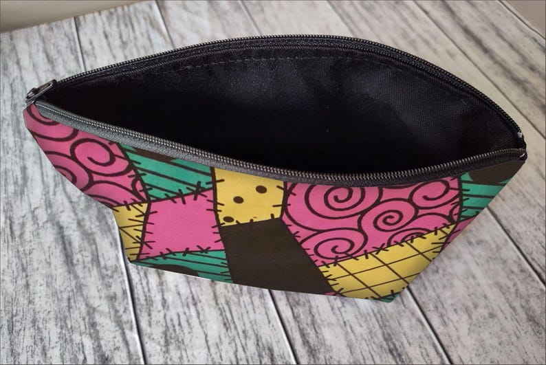 Pu&ograve; includere: Una pochette nera con cerniera con un design a patchwork che presenta tessuto rosa, giallo, verde e marrone. Il tessuto ha un motivo cucito e un design a spirale.