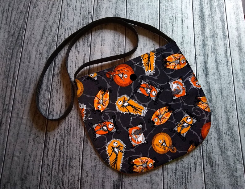 K&ouml;nnte beinhalten: Schwarze Umh&auml;ngetasche mit einem Halloween-Motiv mit Jack Skellington aus Nightmare Before Christmas. Der Druck zeigt orange und wei&szlig;e Jack Skellington-Figuren auf schwarzem Hintergrund.