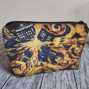May include: A blue and yellow makeup bag featuring a print of the TARDIS from Doctor Who superimposed on a swirling starry night sky, reminiscent of Vincent van Gogh's Starry Night.