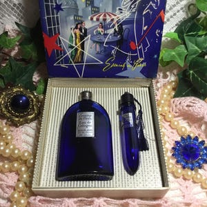 May include: A vintage "Evening in Paris" cologne set in a blue glass bottle and a matching atomizer. The set is presented in a box with a Parisian scene illustration. The cologne bottle is approximately 4 inches tall.
