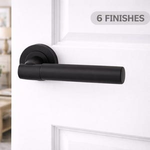 May include: A black door handle with a cylindrical lever and a circular backplate is fixed to a white door. The text "6 FINISHES" is in a grey rectangle above the handle. The background shows a living room.