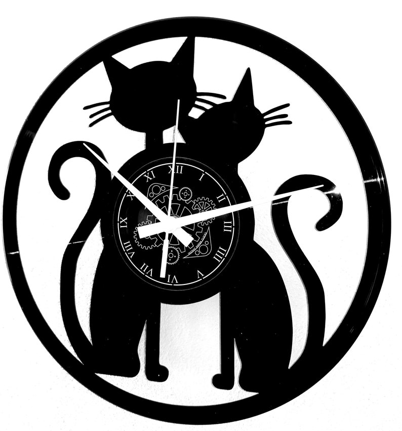 May include: Black cat-themed wall clock. The clock features two cat silhouettes within a circular frame. The clock face has Roman numerals and a gear design. The clock hands are white. The clock is made from a vinyl record.