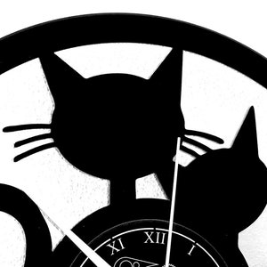 May include: Black and white cat-themed wall clock. The clock features two cat silhouettes and Roman numeral hour markers. The clock hands are visible, indicating the time. The design is simple and modern, suitable for a cat lover's home decor.