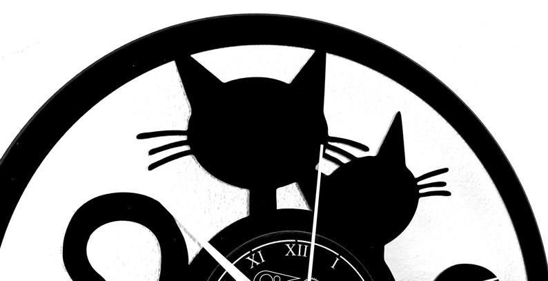 May include: Black and white cat-themed wall clock. The clock features two cat silhouettes and Roman numeral hour markers. The clock hands are visible, indicating the time. The design is simple and modern, suitable for a cat lover's home decor.