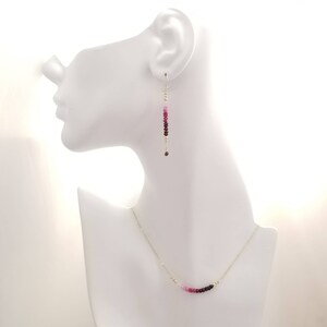 May include: A set of pink and red gemstone earrings and a necklace. The earrings are long and dangle, while the necklace is a delicate chain with a curved row of gemstones.