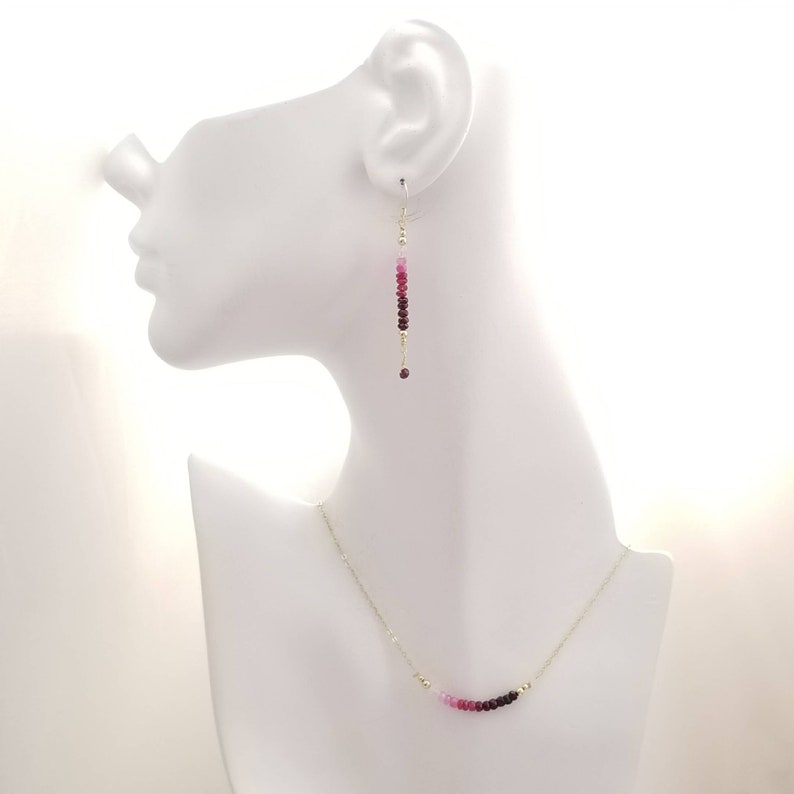 May include: A set of pink and red gemstone earrings and a necklace. The earrings are long and dangle, while the necklace is a delicate chain with a curved row of gemstones.