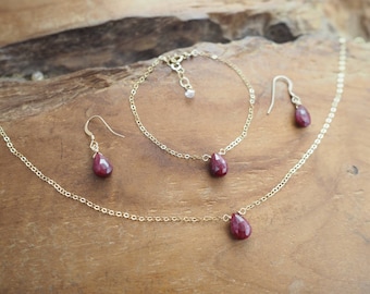 May include: A gold necklace, bracelet, and earrings set with teardrop-shaped ruby gemstones.