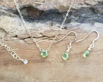 May include: A set of delicate silver jewelry featuring light green peridot gemstones. The set includes a necklace with a single peridot pendant and a pair of matching earrings.