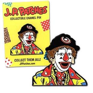 May include: A yellow, red, and blue enamel pin of a clown with a black hat and a red nose. The pin says "J.P. Patches" and "Collect Them All! JPPatches.com".
