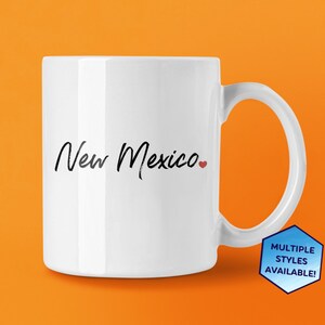 May include: White ceramic coffee mug with black text that reads "New Mexico" and a small red heart.