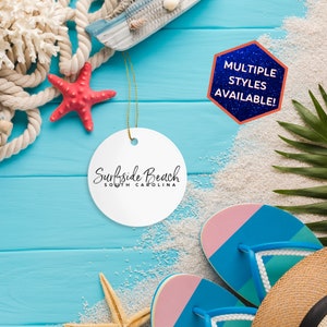 May include: White round ornament with the text "Surfside Beach South Carolina" on a blue wooden background with beach-themed decorations, including seashells, starfish, rope, and flip-flops. The text "Multiple Styles Available!" is on a blue hexagon with a glittery texture.