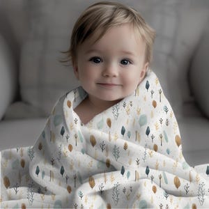 Könnte beinhalten: Ein Baby, eingewickelt in eine weiche, weiße Decke mit einem Muster aus kleinen grünen und gelben Bäumen und Blättern.