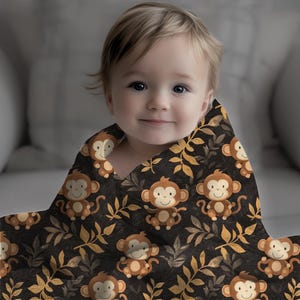 May include: A baby swaddled in a soft, brown and yellow blanket with a pattern of monkeys and leaves. The blanket is made of a plush material and is perfect for keeping a baby warm and cozy.