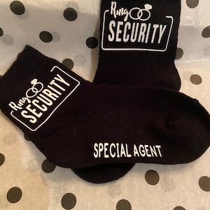 May include: A pair of black socks with white text. One sock says "Ring Security" with a ring and diamond graphic. The other sock says "Special Agent".