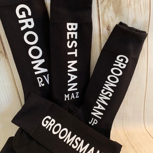 May include: Three black socks with white text. The socks say "Groom", "Best Man", and "Groomsman".