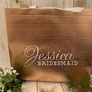 Puede incluir: Una bolsa de tela reutilizable de color oro rosa con el texto "Jessica Bridesmaid" impreso en blanco.