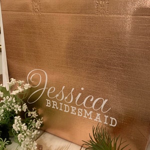 Puede incluir: Una bolsa de tela reutilizable de color oro rosa con el nombre "Jessica Bridesmaid" impreso en blanco.