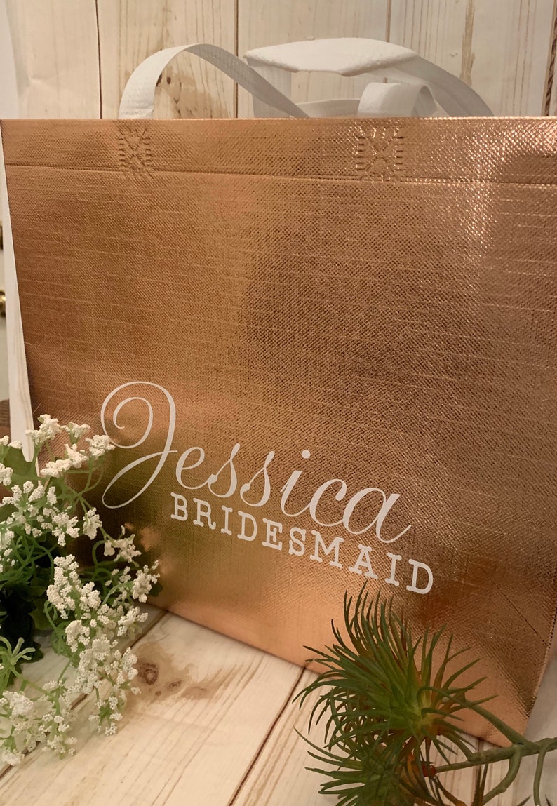 Puede incluir: Una bolsa de tela reutilizable de color oro rosa con el nombre "Jessica Bridesmaid" impreso en blanco.