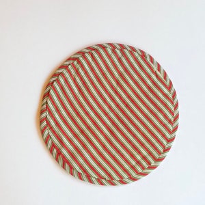 Op de afbeelding: Ronde placemat van stof met rode en groene strepen.