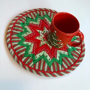 Op de afbeelding: Een rode en groene kerst-themadessert met een stervormig ontwerp. Een rode mok met een wit kerstboomontwerp staat op de onderzetter.