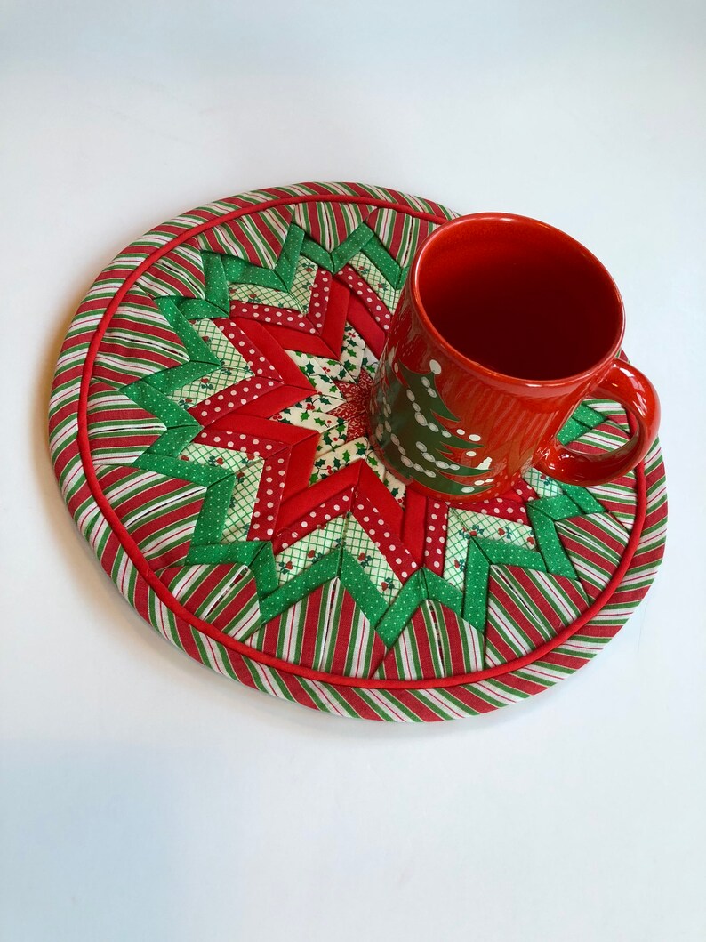 Op de afbeelding: Een rode en groene kerst-themadessert met een stervormig ontwerp. Een rode mok met een wit kerstboomontwerp staat op de onderzetter.