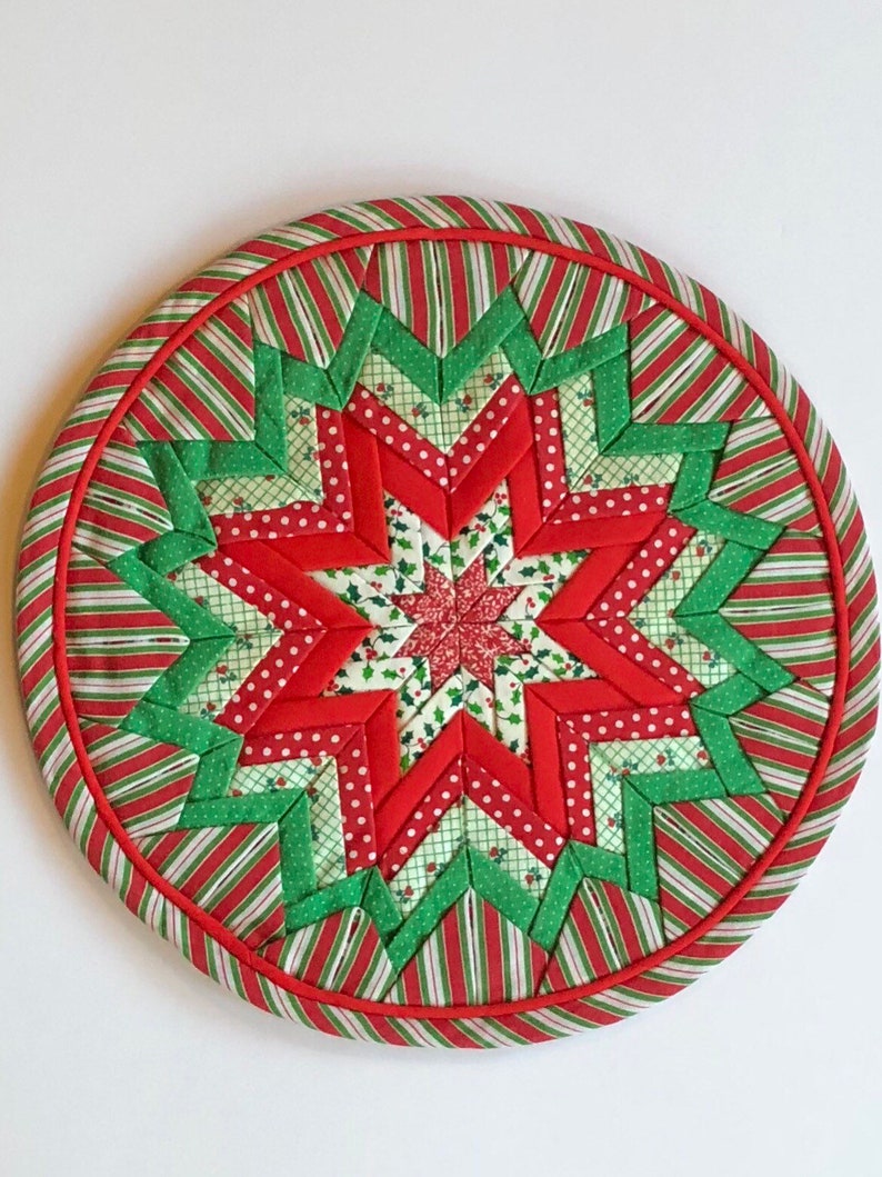 Op de afbeelding: Een ronde, rode, groene en witte gestikte kerstversiering met een stervorm.
