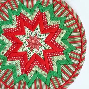 Op de afbeelding: Een ronde, rode en groene gestikte kerstversiering met een stervorm. De ster is gemaakt van rood en groen stof met witte stippen.