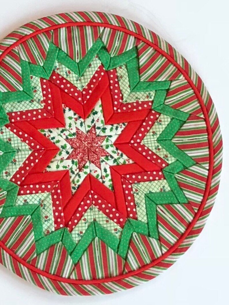 Op de afbeelding: Een ronde, rode en groene gestikte kerstversiering met een stervorm. De ster is gemaakt van rood en groen stof met witte stippen.