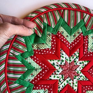 Op de afbeelding: Een rode en groene kerst-theedoek met een stervormig ontwerp. De theedoek is gemaakt van stofresten in verschillende patronen, waaronder stippen, strepen en hulst.