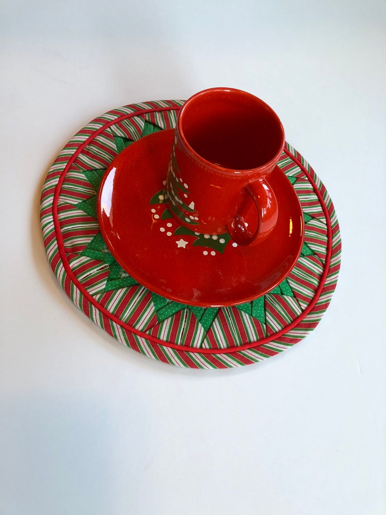 Op de afbeelding: Rode en groene kerst-thema stoffen placemat met een rode schotel en een rode mok met een wit kerstboomontwerp.