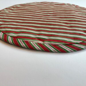 Op de afbeelding: Ronde placemat met rode en groene strepen met witte strepen. De placemat is gemaakt van stof en heeft een gestikte rand.