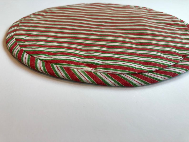 Op de afbeelding: Ronde placemat met rode en groene strepen met witte strepen. De placemat is gemaakt van stof en heeft een gestikte rand.