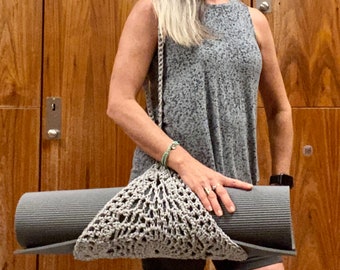 May include: A gray crocheted yoga mat bag with a gray yoga mat inside. The bag has a long strap that goes over the shoulder.