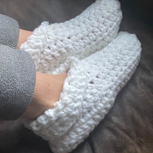 May include: White crocheted slippers with a folded cuff. The slippers are made with a chunky yarn and have a simple, cozy design.