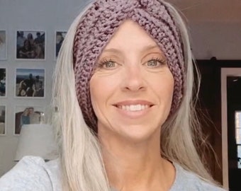 May include: A woman with long, silver hair is wearing a purple crocheted headband. The headband is twisted and has a criss-cross pattern.