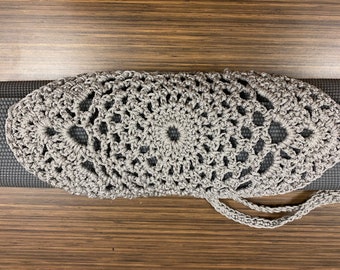 May include: A gray crocheted yoga mat carrier with a drawstring closure. The carrier is made of a delicate, openwork pattern and has a simple, elegant design.