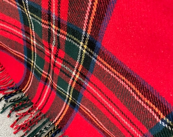 May include: A red plaid blanket with a fringed edge. The blanket features a classic tartan pattern with black, green, yellow, and white stripes. The blanket is folded, showing the pattern and texture of the fabric.