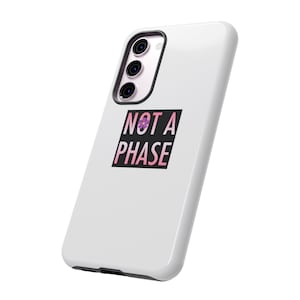 Puede incluir: Carcasa de teléfono blanca con un cuadrado negro que dice "NOT A PHASE" en letras rosa y blancas con una pequeña flor morada en el medio de la "A".