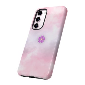 Puede incluir: Una funda de teléfono rosa y blanca con un patrón de nubes y una pequeña flor morada. La funda tiene una protuberancia de cámara negra con tres lentes.