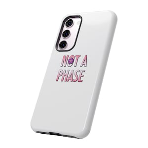 Puede incluir: Carcasa de teléfono blanca con un gráfico rosa y morado que dice "NOT A PHASE" con una pequeña flor morada.