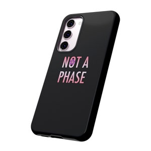 Puede incluir: Carcasa de teléfono negra con una flor rosa y morada y el texto "NOT A PHASE" en rosa.