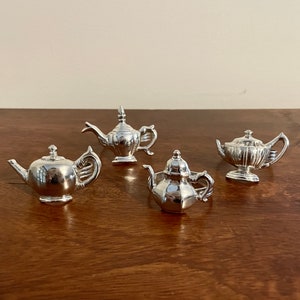 Könnte beinhalten: Vier silberne Teekannen-Serviettenringe. Die Serviettenringe haben alle unterschiedliche Designs und sind aus glänzendem Metall gefertigt.