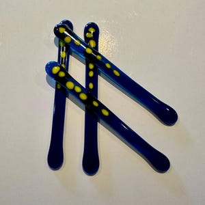 Può includere: Tre bastoncini di vetro blu con pois gialli.