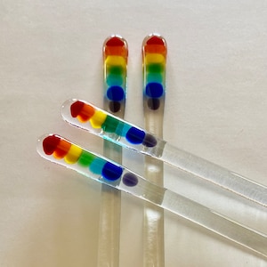 May include: Three clear glass stirring sticks with rainbow colored glass beads at the top. The beads are red, orange, yellow, green, blue, and purple.