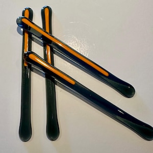 May include: Three glass stirring sticks with rounded ends. The sticks are dark gray with a single orange stripe down the center.