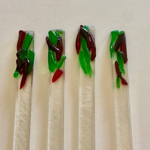 May include: Four glass sticks with red, green, and black glass pieces fused onto the surface. The sticks are clear glass and the fused pieces are arranged in a random pattern.
