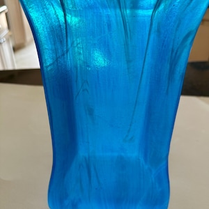 Puede incluir: Primer plano de un objeto translúcido azul brillante con forma curva. El objeto tiene una superficie lisa con sutiles vetas de azul claro y blanco, creando un efecto marmolado. La base es de forma rectangular sólida.