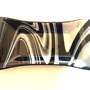 Könnte beinhalten: Ein rechteckiger Teller aus Glas in Schwarz und Weiß mit einem wellenförmigen Marmormuster. Der Teller hat eine leicht geschwungene Form und ist vor einem weißen Hintergrund platziert. Das Schwarz-Weiß-Muster erzeugt einen auffälligen visuellen Effekt.