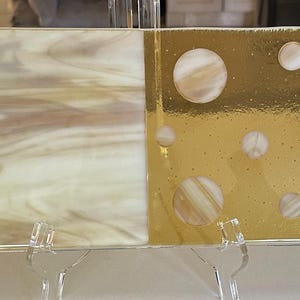 May include: A rectangular decorative glass piece with three distinct sections. The left and right sections feature a swirling, marbled pattern in cream and tan. The center section is gold with white and tan circles. The edges are trimmed with a thin gold border.