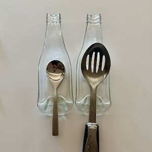 May include: Two clear glass bottle spoon rests with a silver slotted spoon and a silver spoon inside.